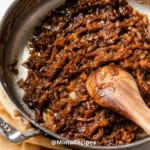 Homemade caramelized onions cooking in a skillet with a wooden spoon until rich, golden brown and perfectly tender.