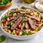 The image showcases a vibrant steak pasta salad with juicy sliced sirloin, fresh vegetables, and Parmesan in a bright, modern setting with clean natural light.