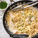 Overhead view of creamy Chicken Alfredo with tender sliced chicken breast, fettuccine pasta coated in rich Parmesan Alfredo sauce, fresh parsley, and kitchen tongs in a black skillet.