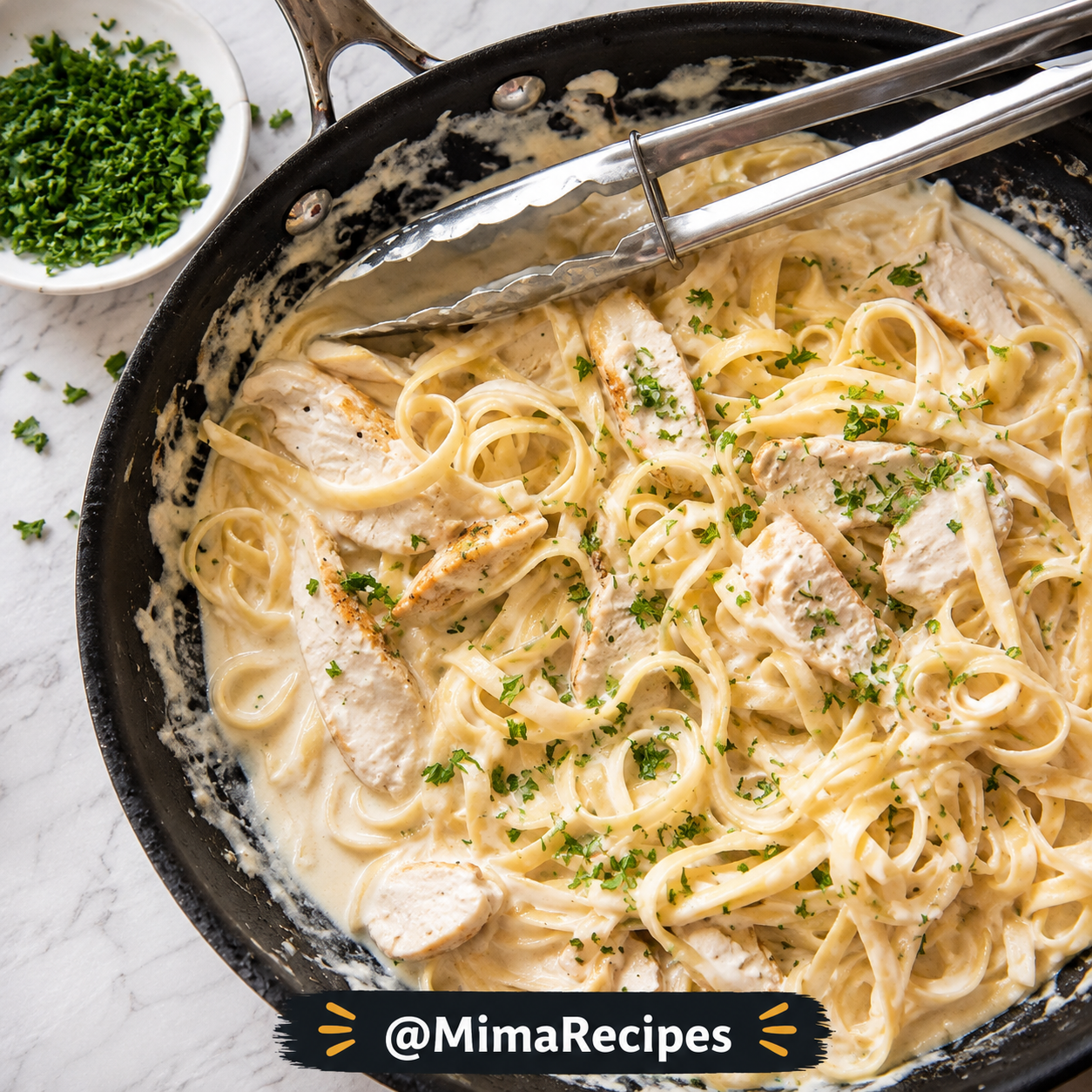 Overhead view of creamy Chicken Alfredo with tender sliced chicken breast, fettuccine pasta coated in rich Parmesan Alfredo sauce, fresh parsley, and kitchen tongs in a black skillet.
