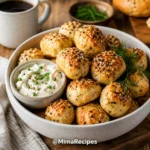 Golden brown Greek Yogurt Bagel Bites topped with everything bagel seasoning served in a white bowl with whipped cream cheese and fresh herbs.