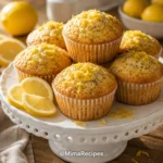 Bakery-style Lemon Poppyseed Muffins with golden domed tops on a white ceramic cake stand, garnished with fresh lemon slices and lemon zest.