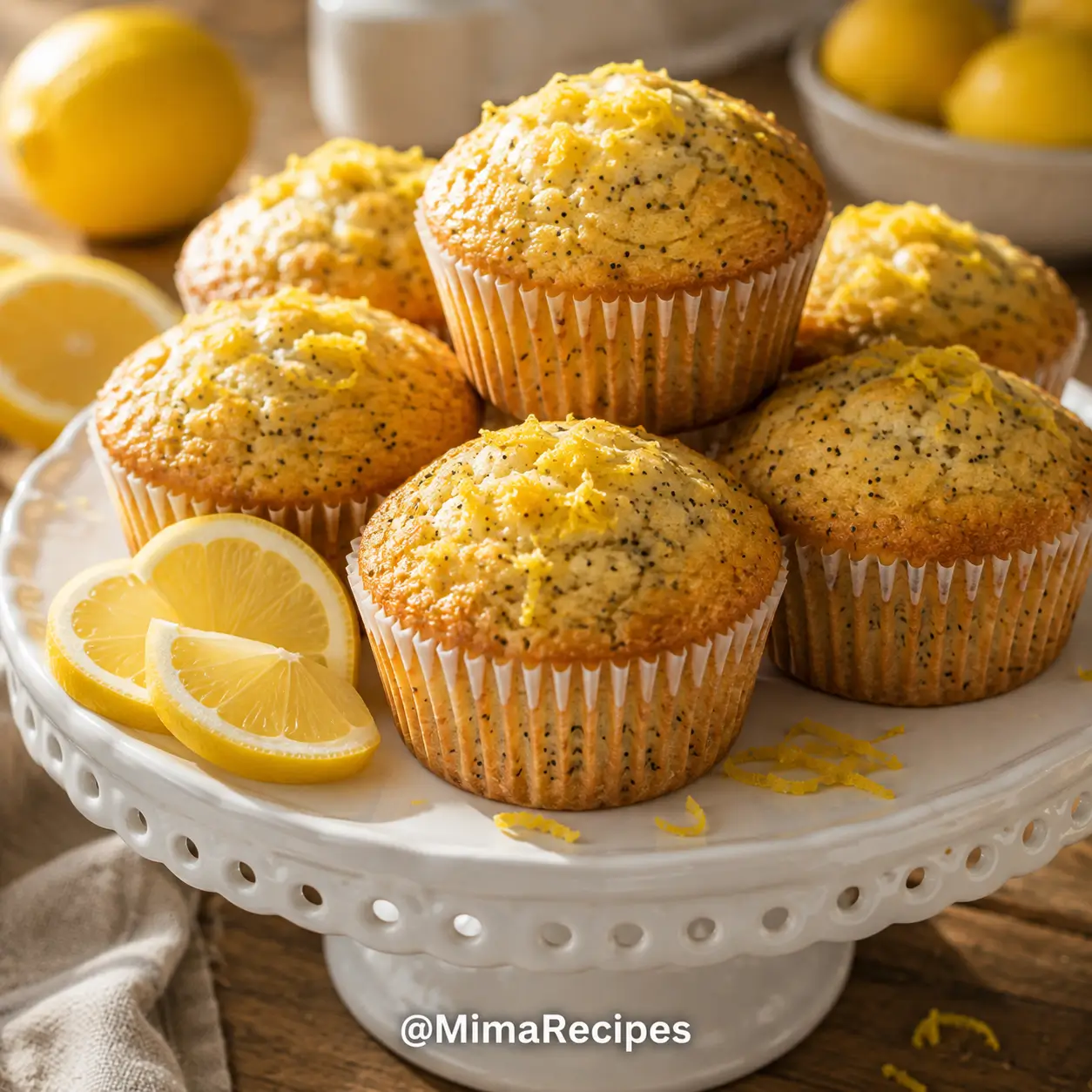 Bakery-style Lemon Poppyseed Muffins with golden domed tops on a white ceramic cake stand, garnished with fresh lemon slices and lemon zest.